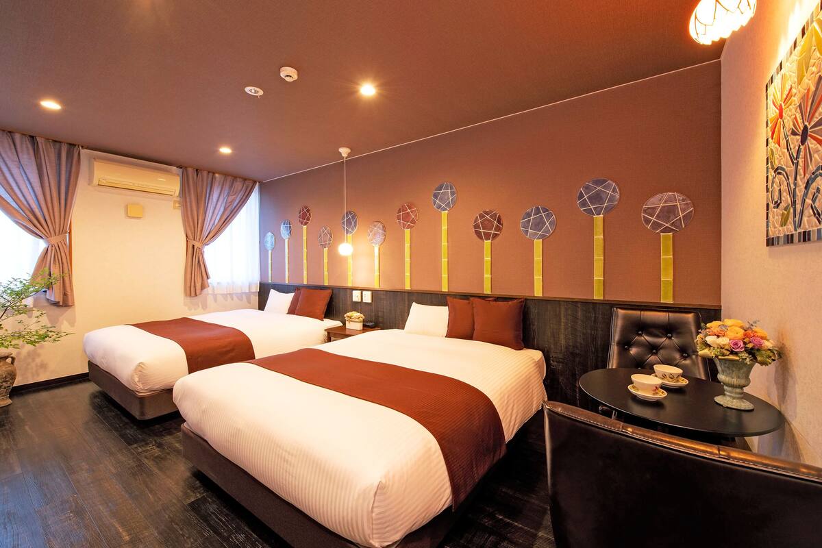 A hotel room with two beds, a dining table, and a decorative wall with circular patterns.