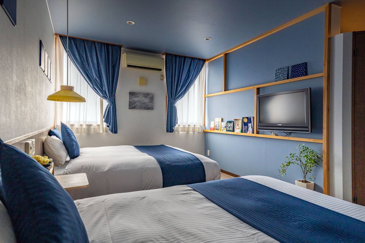 A hotel room with two beds, a TV on the wall, and a small plant.