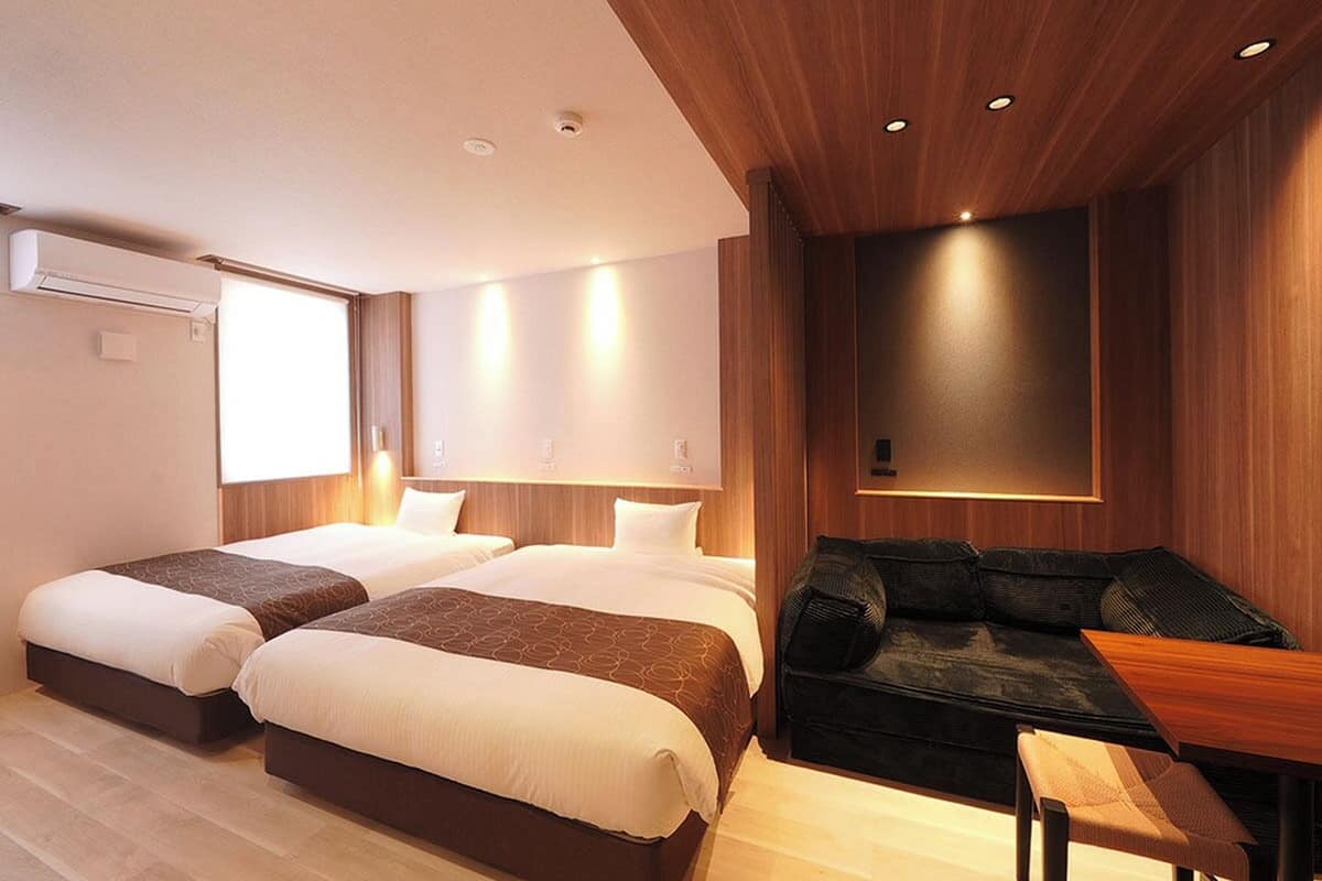 A hotel room with a large bed, a sofa, a small table, and a wall-mounted TV.