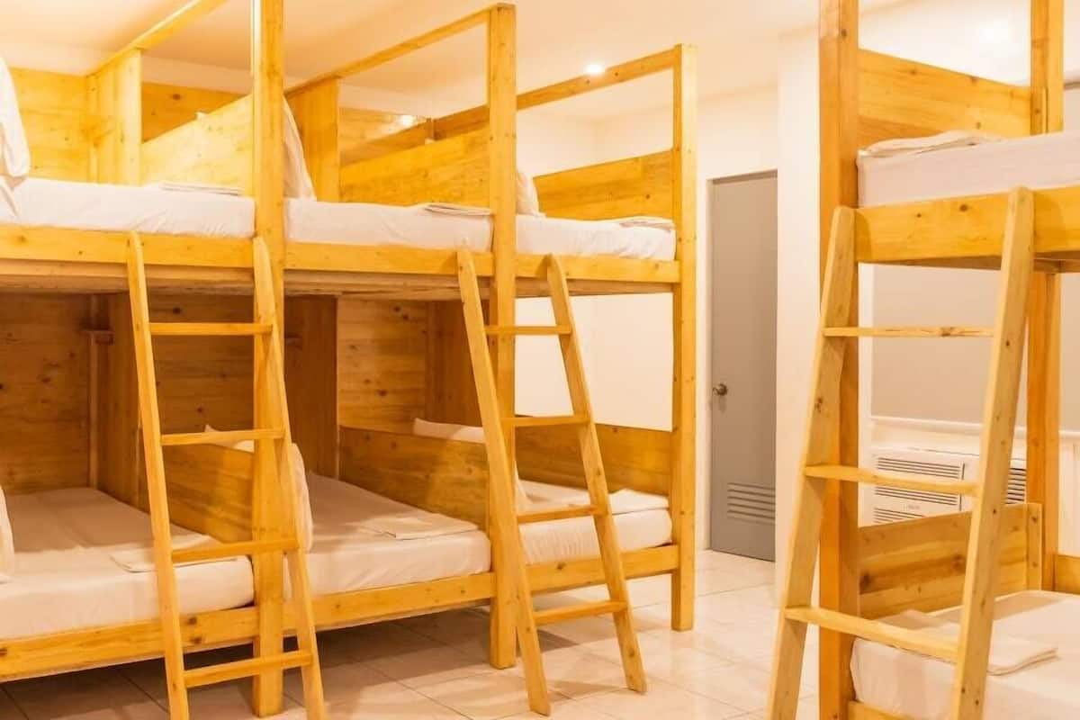 A room with three wooden bunk beds, each with a ladder and white bedding.