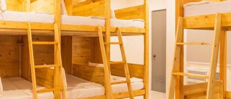 Una habitación con tres literas de madera, cada una con una escalera y ropa de cama blanca.