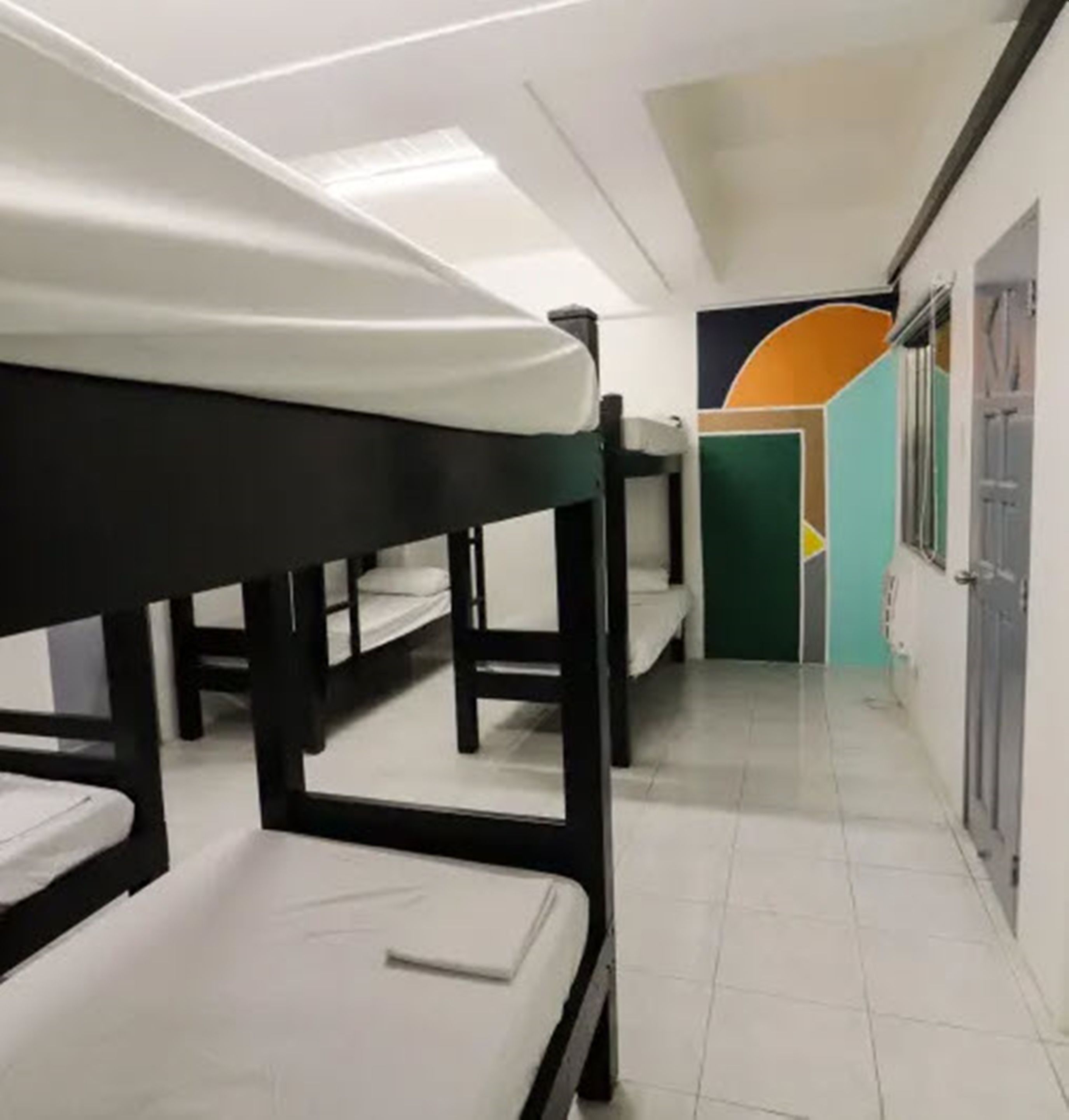 A dormitory room with bunk beds, a tiled floor, and a door with a geometric mural.