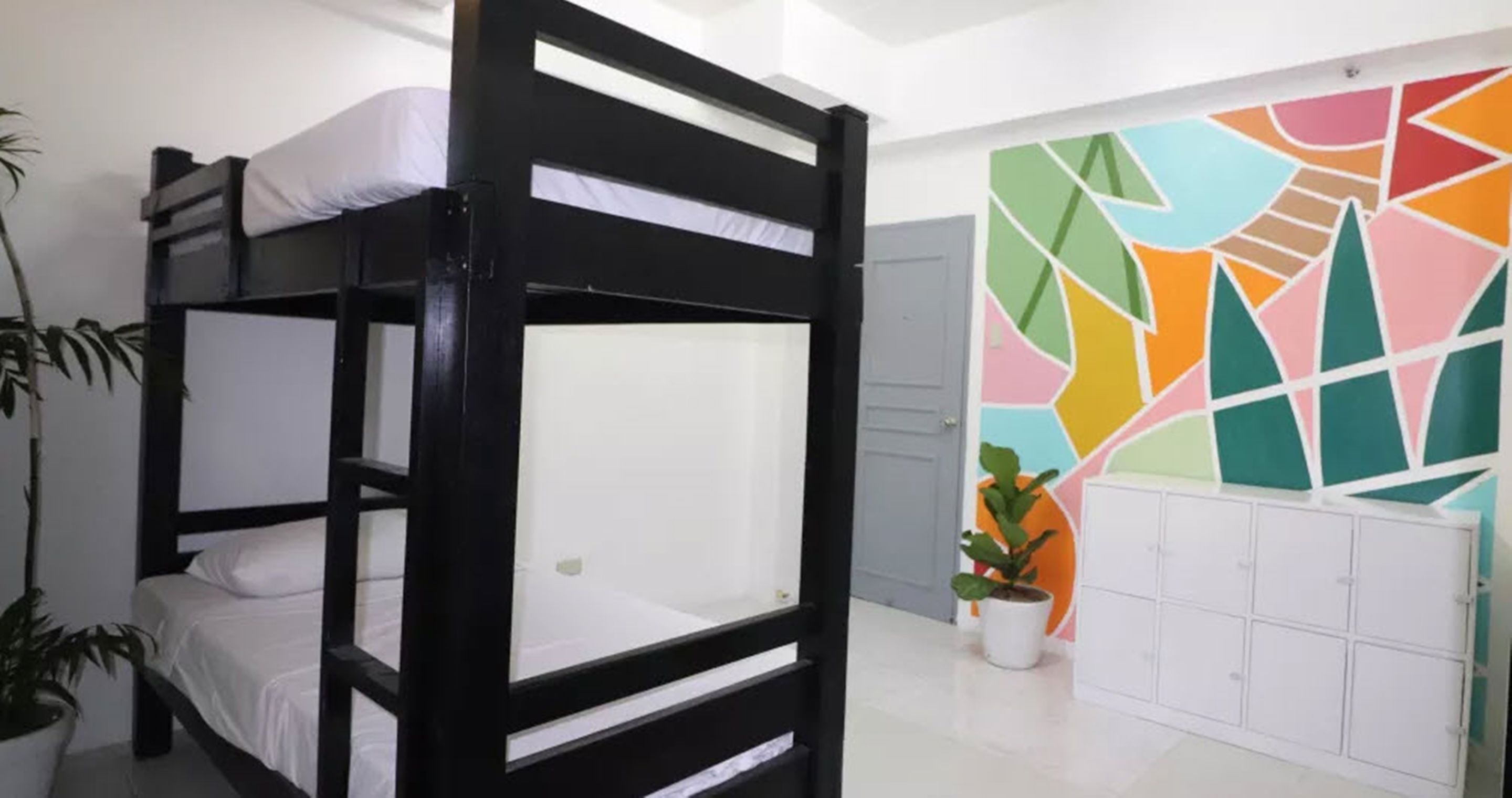 A bunk bed room with a colorful abstract wall mural, a potted plant, and a white cabinet.