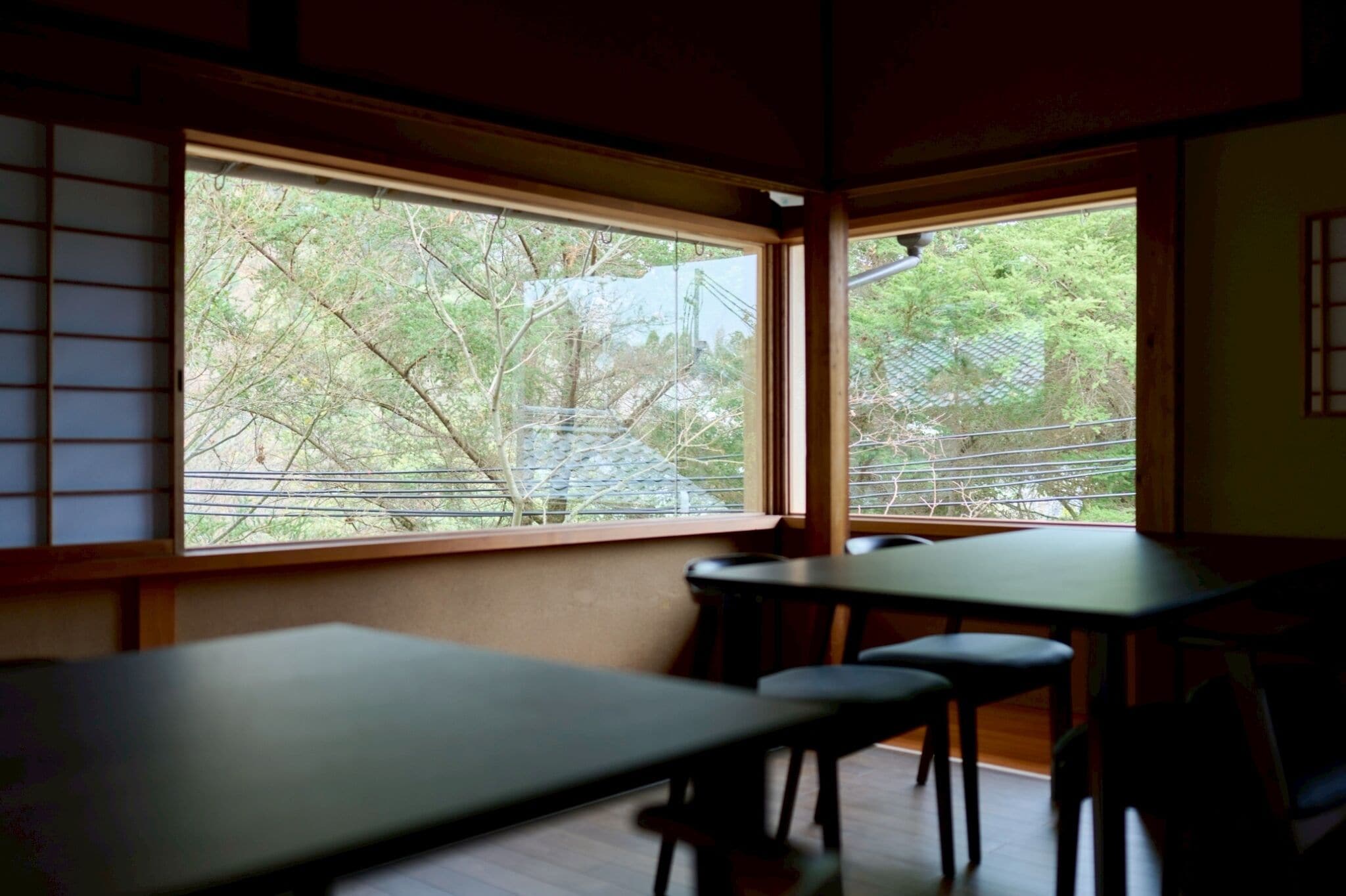 A room with a low table and chairs, large windows with a view of trees and a fence.