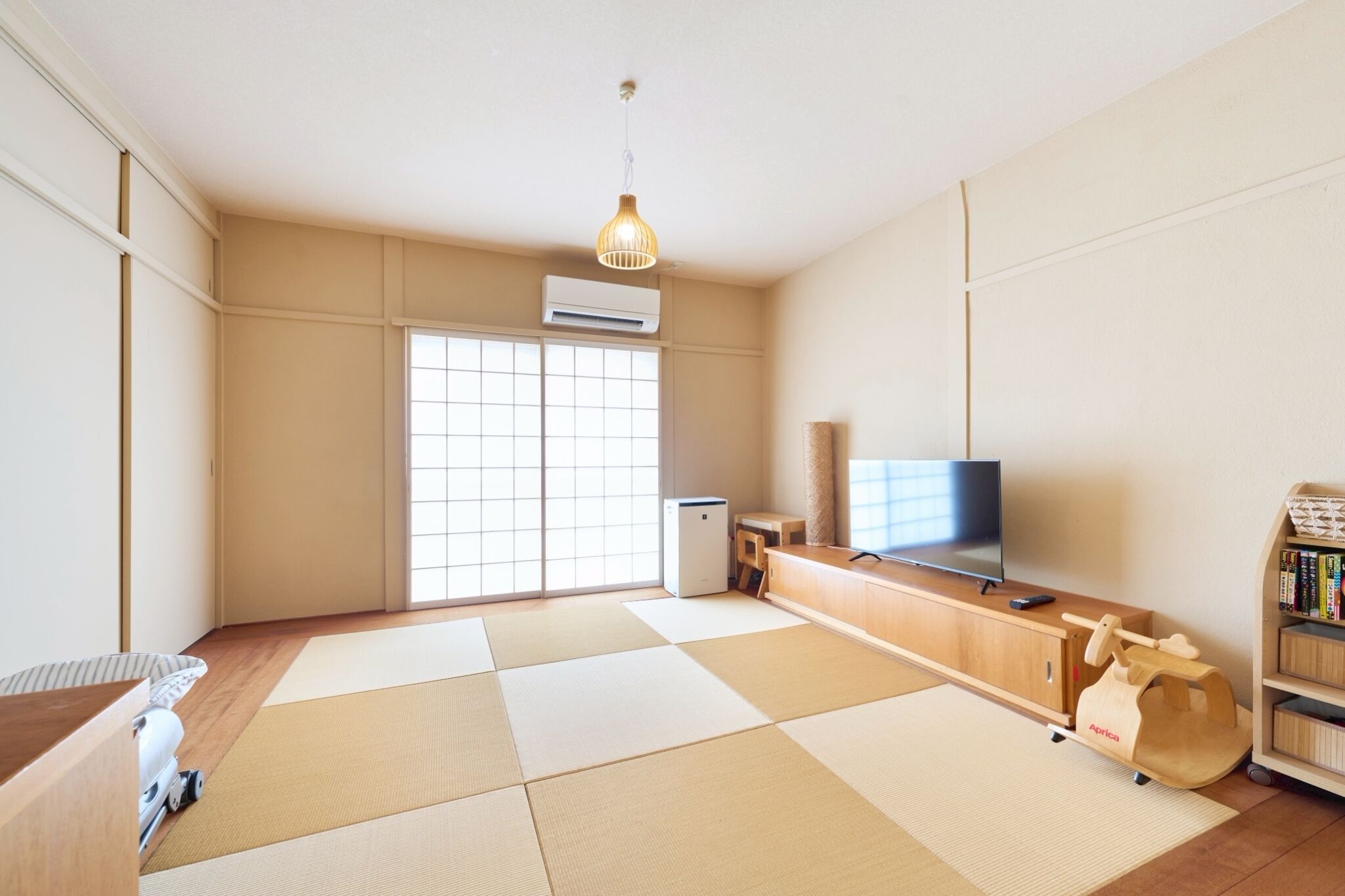 A minimalist living room with tatami mats, a television, a small refrigerator, and a bookshelf.