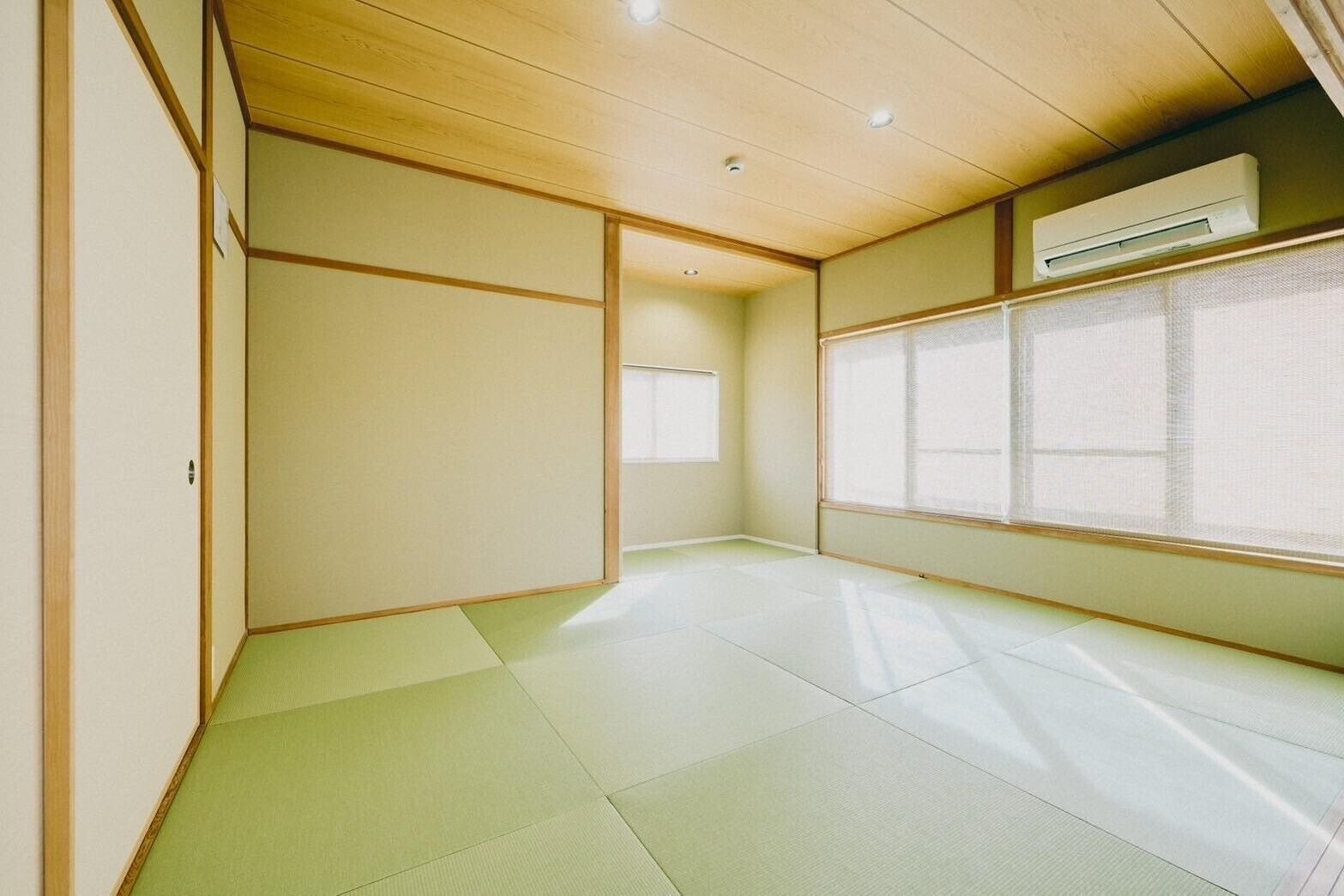 A room with tatami flooring, sliding doors, a window with a view, and an air conditioning unit.
