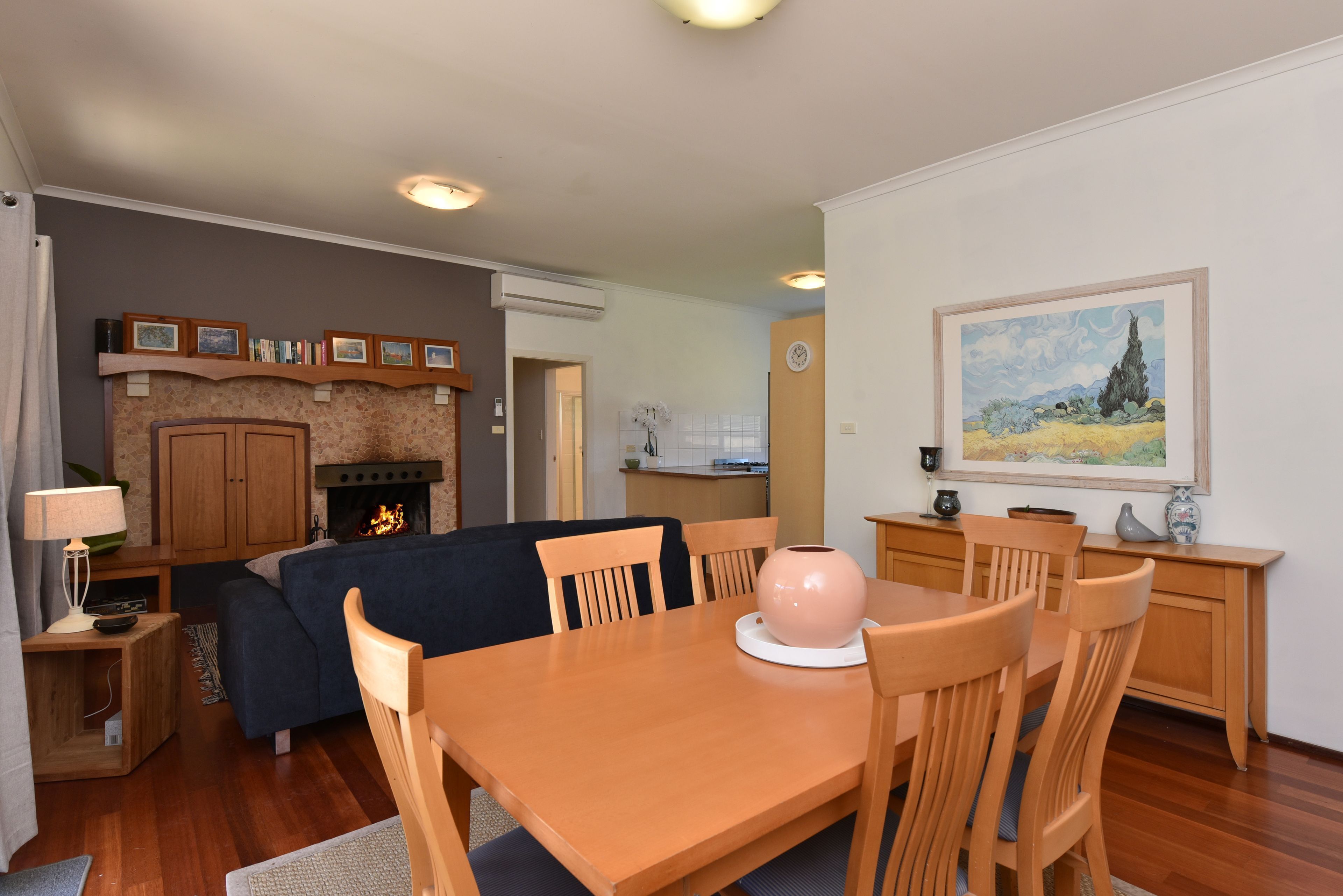 Un salon avec une cheminée, une table à manger avec des chaises, un coin cuisine et un tableau accroché au mur.
