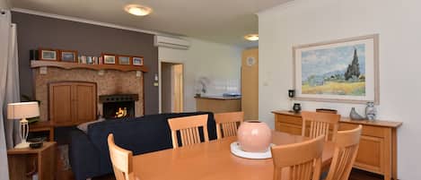 Un salon avec une cheminée, une table à manger avec des chaises, un coin cuisine et un tableau accroché au mur.