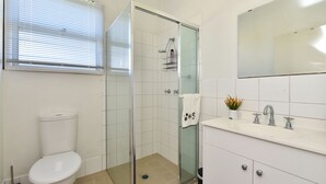 Moderni kylpyhuone, jossa on wc, lasinen suihkuseinä ja peilillä varustettu pesuallas.