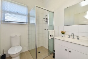 Moderni kylpyhuone, jossa on wc, lasinen suihkuseinä ja peilillä varustettu pesuallas.