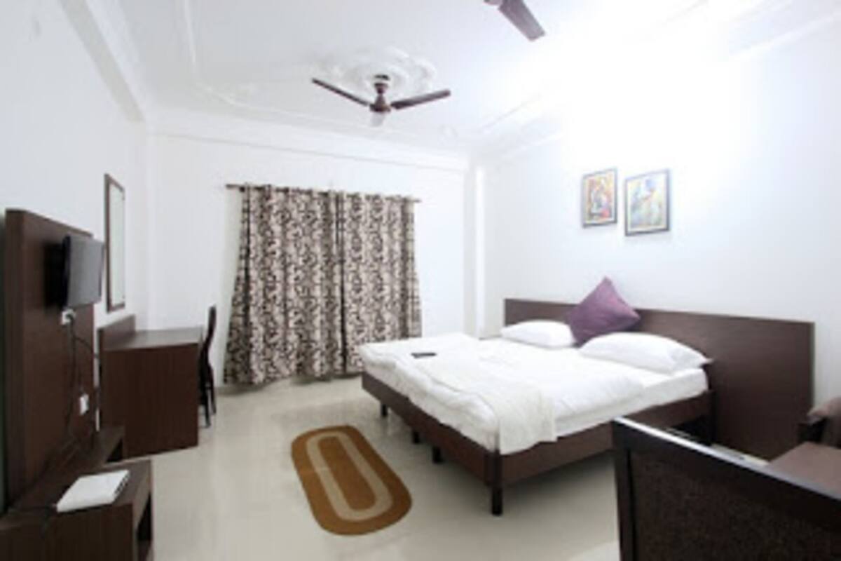 A hotel room with a bed, a desk, a chair, a television, and a ceiling fan.