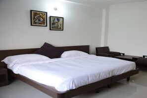 Quarto de hotel moderno com uma cama grande, uma mesinha de cabeceira, uma cadeira e duas obras de arte emolduradas na parede.