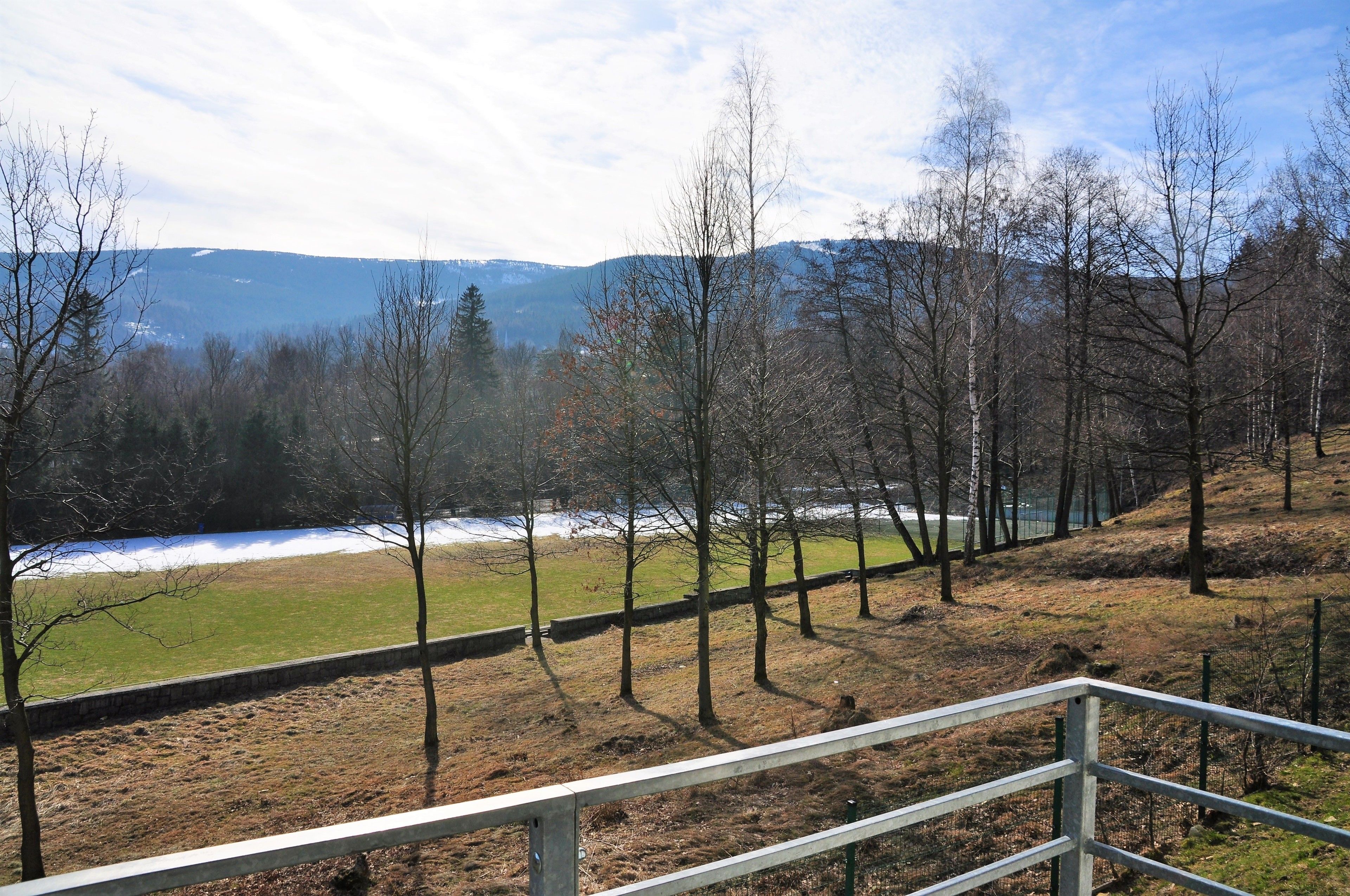 A view of a river with a stone wall and trees in the foreground, and mountains in the background.