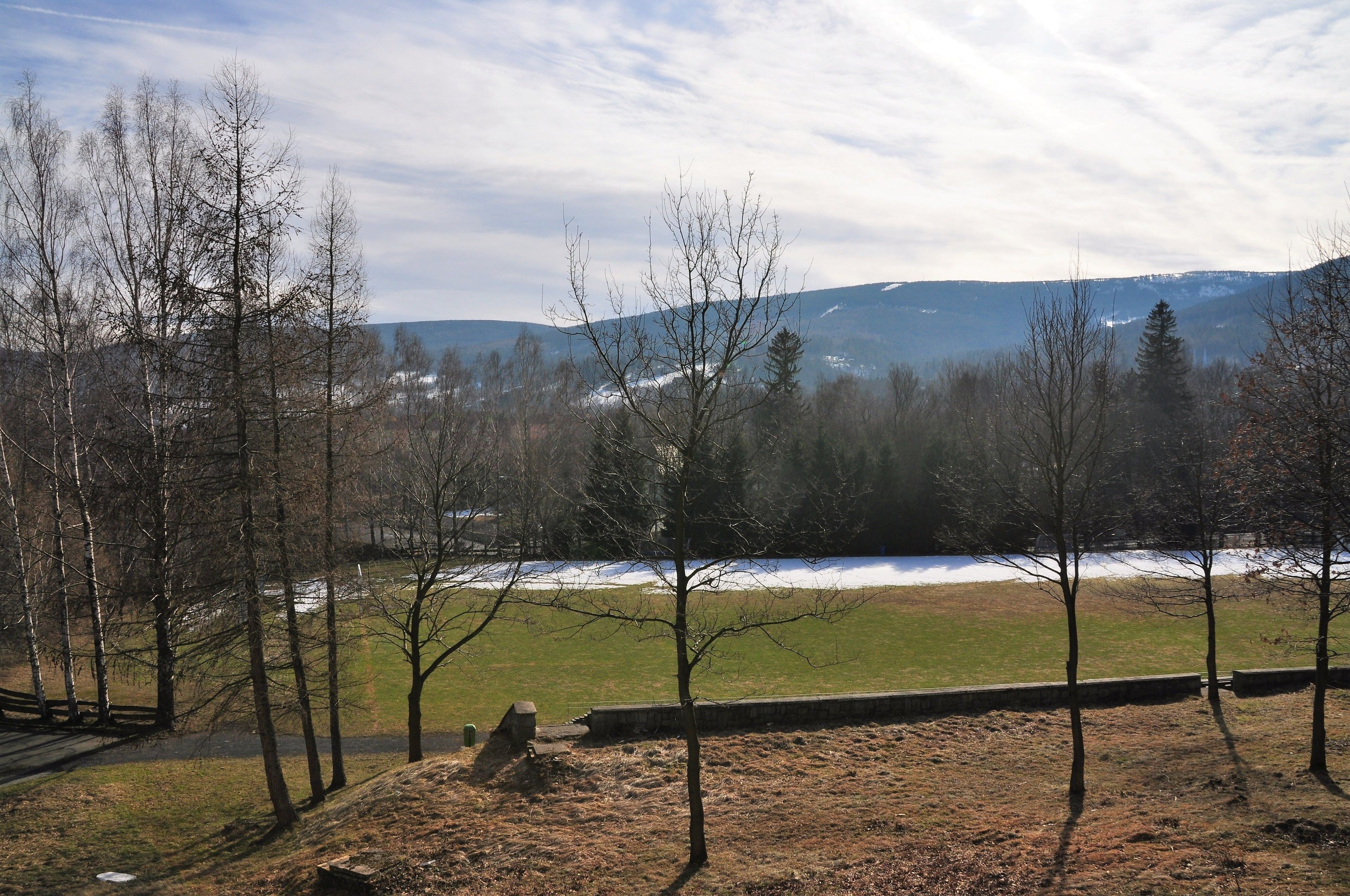 A park with a grassy area, trees, and a view of distant mountains.