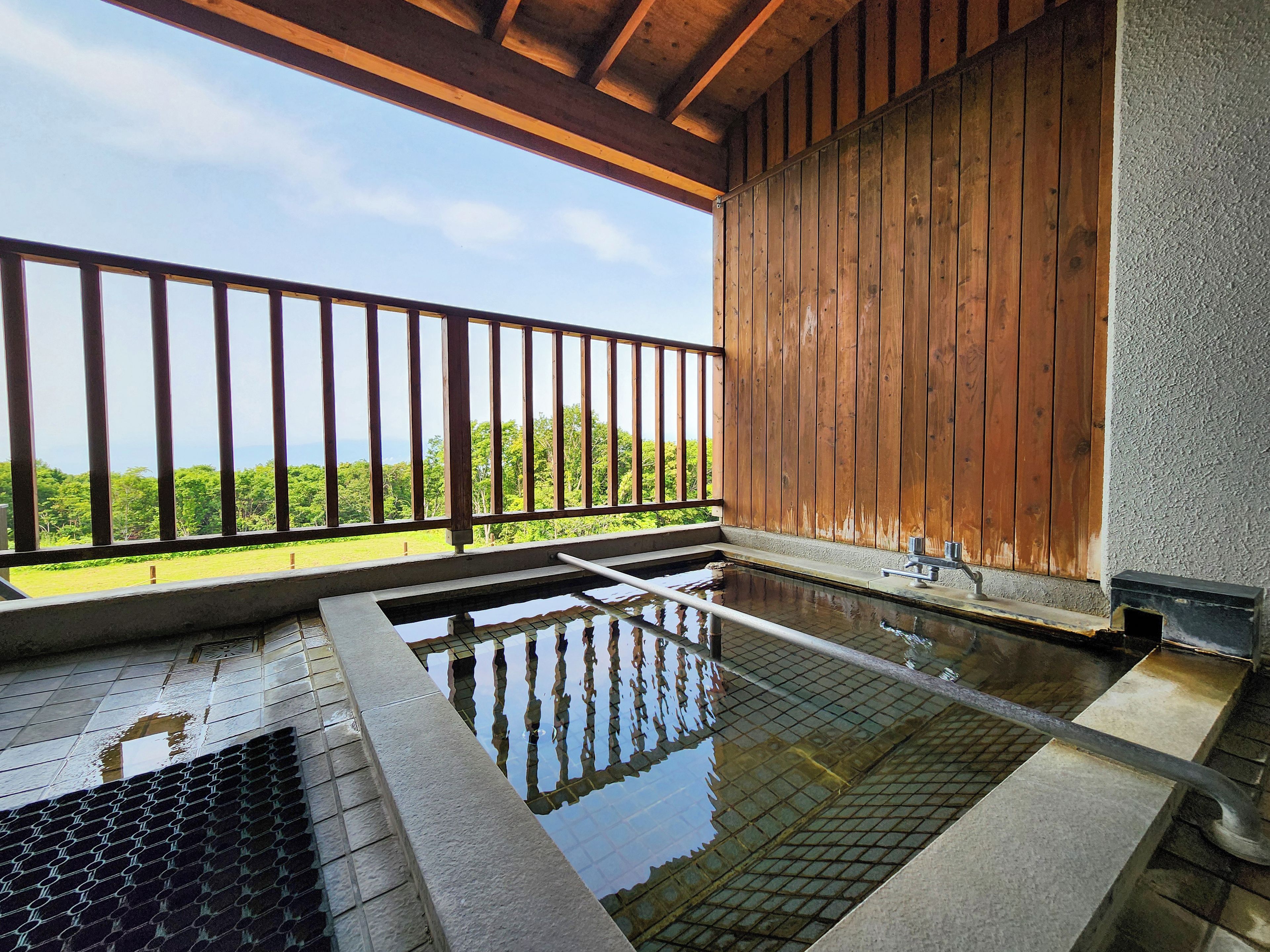 A traditional Japanese onsen with a wooden deck and a view of lush greenery.