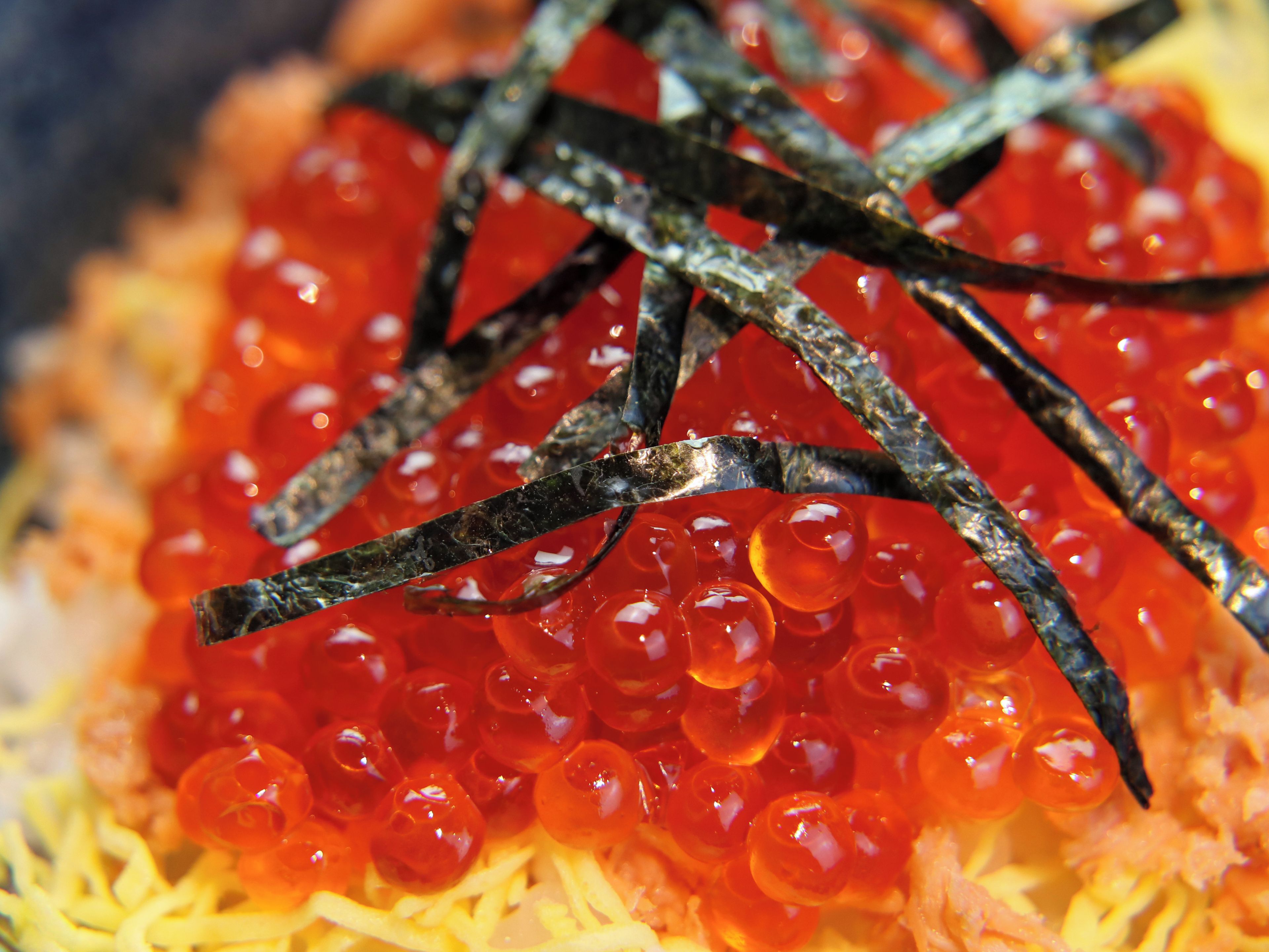 A close-up of red caviar on a bed of shredded yellow cheese with dark, thin strips on top.