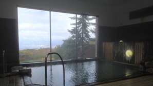 An indoor swimming pool with a view of trees and mountains through large windows. - Iwanai Kogen Hotel (Iwanai)
