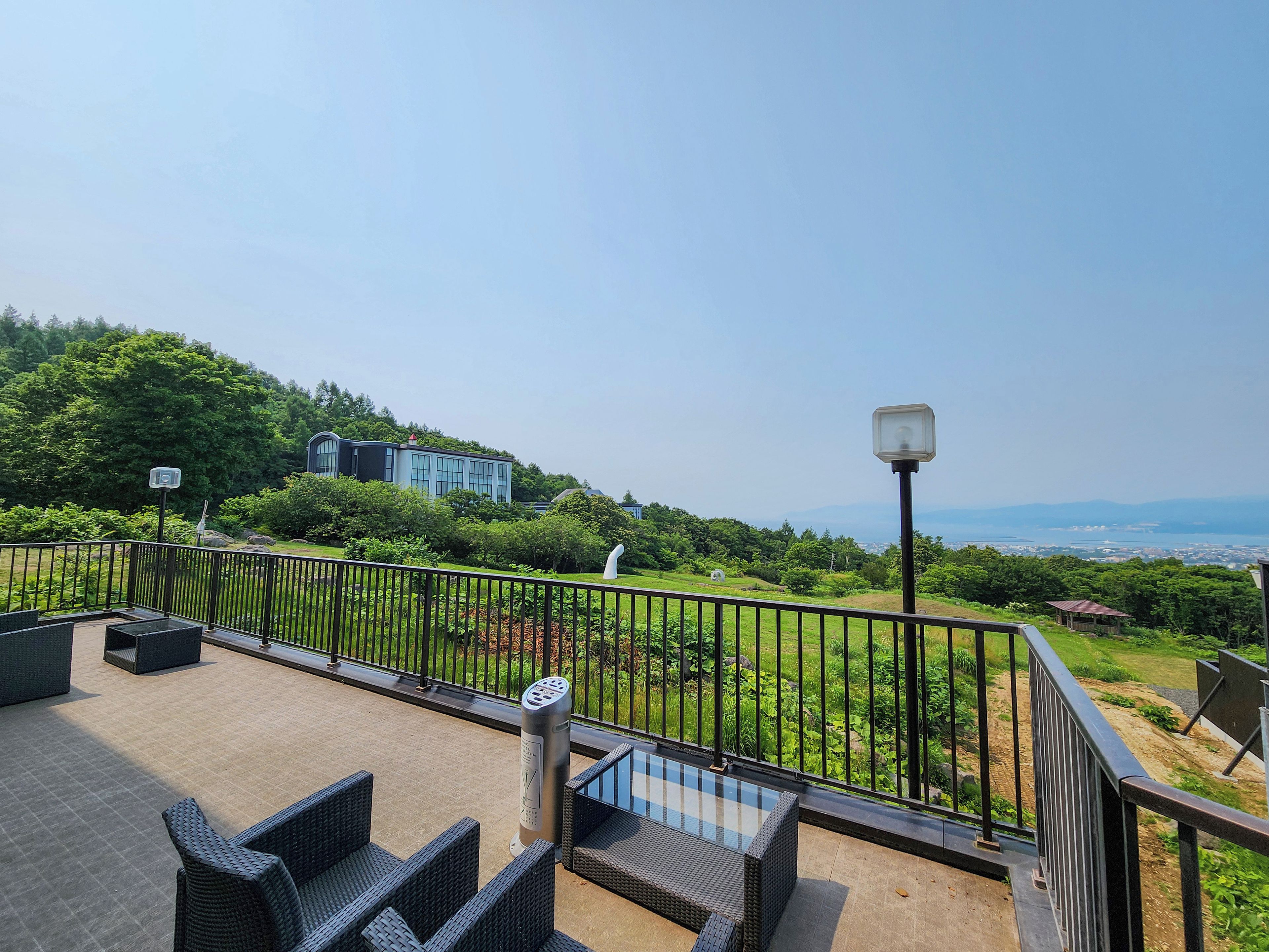 A rooftop terrace with outdoor furniture, a metal railing, and a view of a cityscape and hills in the distance.