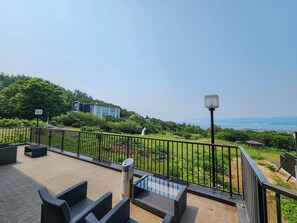 A rooftop terrace with outdoor furniture, a metal railing, and a view of a cityscape and hills in the distance. - Iwanai Kogen Hotel (Iwanai)