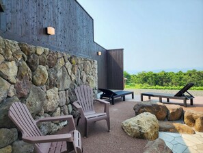 An outdoor seating area with Adirondack chairs and a flat-screen TV against a stone wall, overlooking a lush landscape. - Iwanai Kogen Hotel (Iwanai)