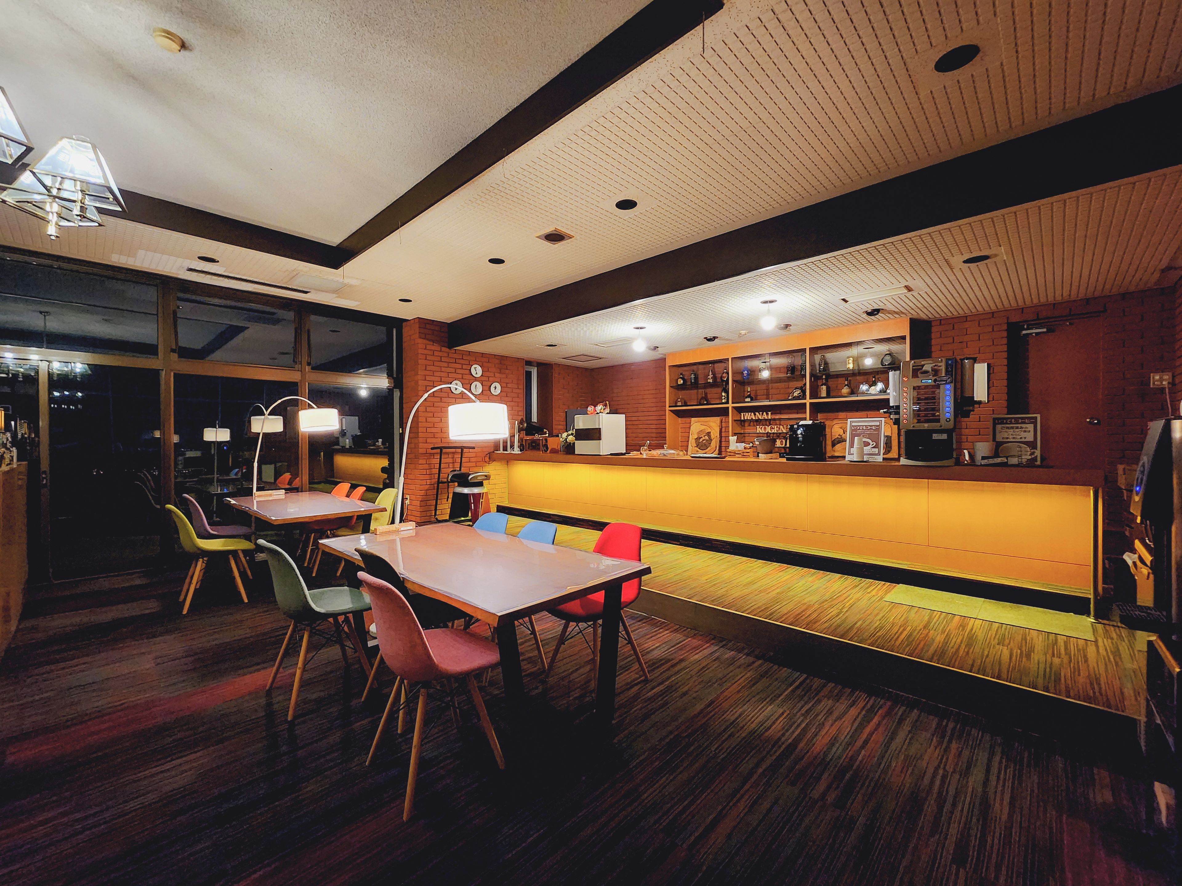 Un interior de restaurante con suelo de madera, una barra con caja registradora y varias mesas con sillas.