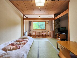 A room with a bed, a wooden table, a TV, and a window with a view of trees. - Iwanai Kogen Hotel (Iwanai)