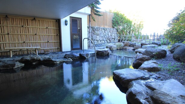 A stone hot spring with a wooden fence and a building with a door and window. - Iwanai Kogen Hotel (Iwanai)