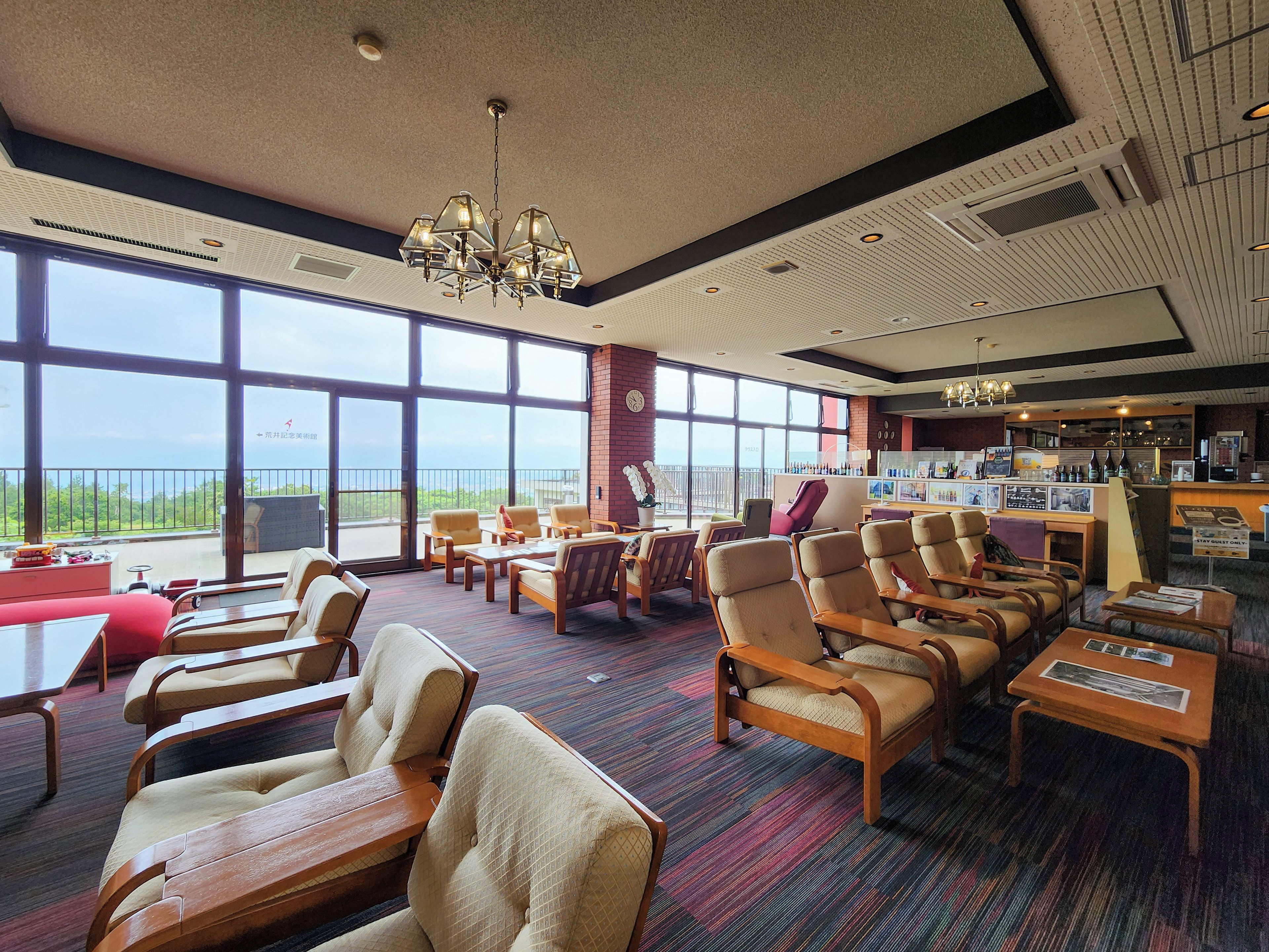 A hotel lobby with a large window offering a view of the sea, multiple seating areas, and a bar.