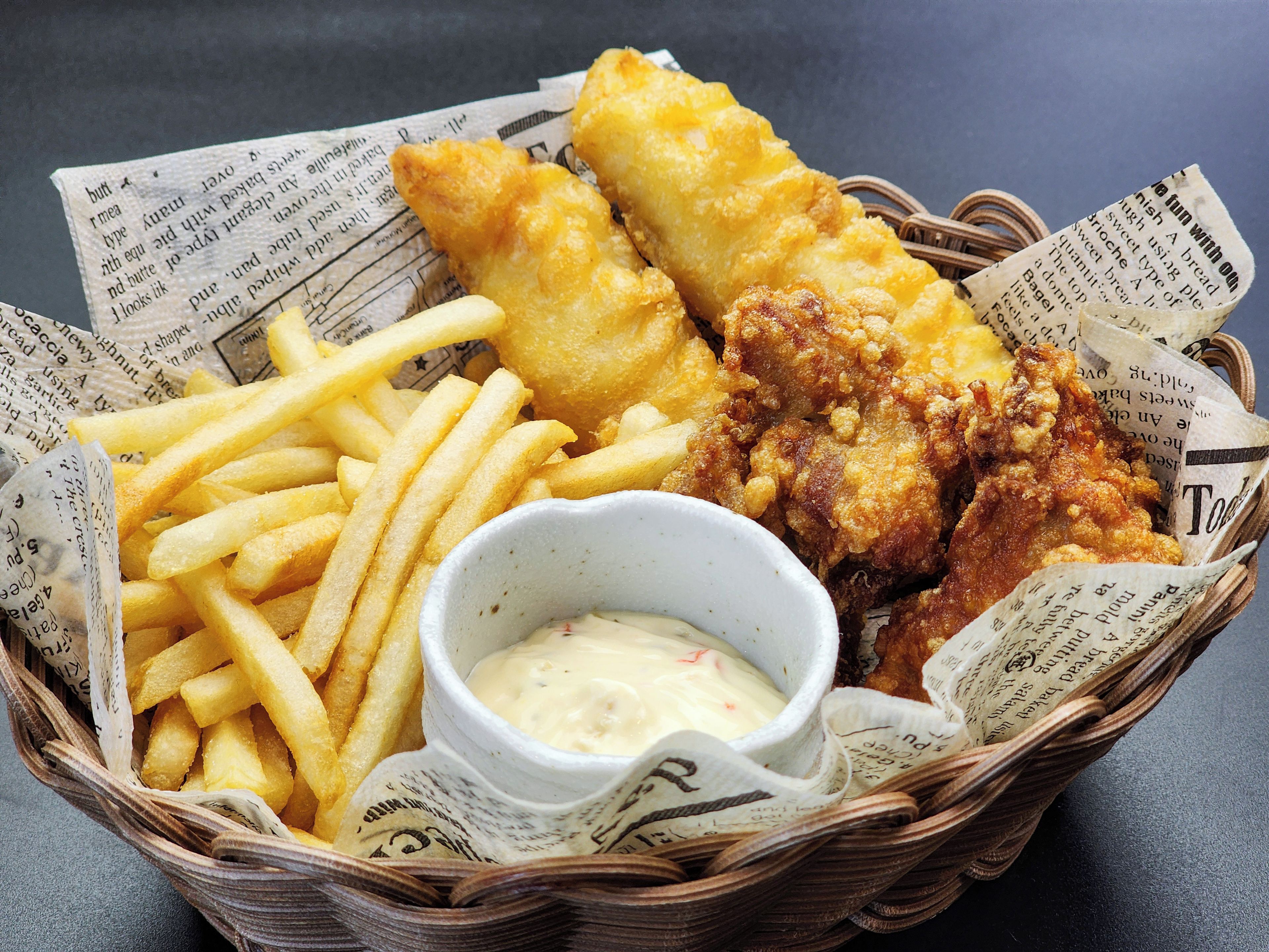 A basket containing fish and chips, a small bowl of sauce, and a newspaper.