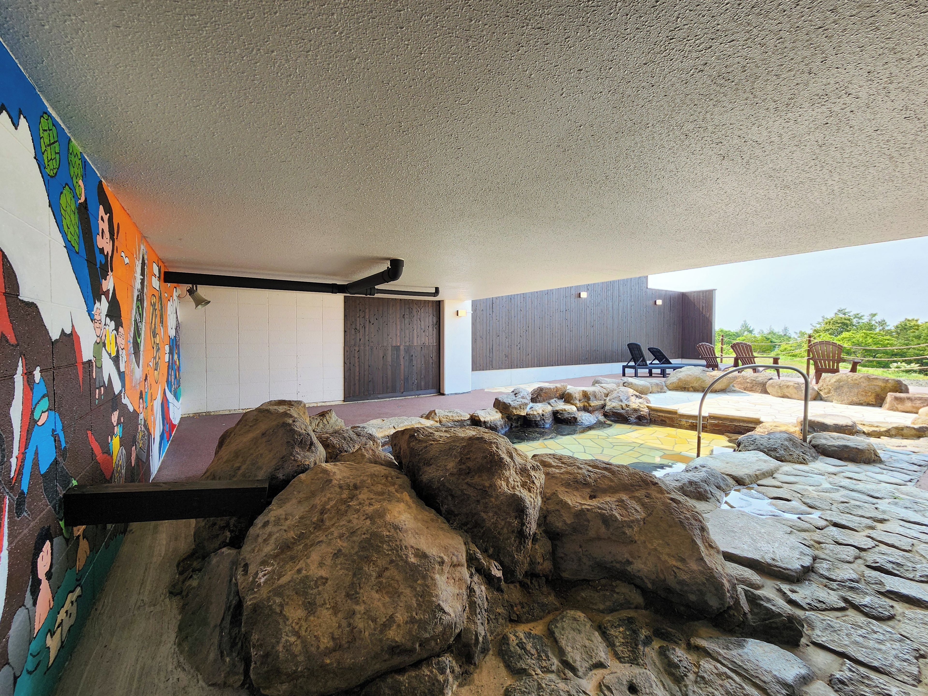 A modern interior with a stone water feature, a mural, and a seating area with lounge chairs.