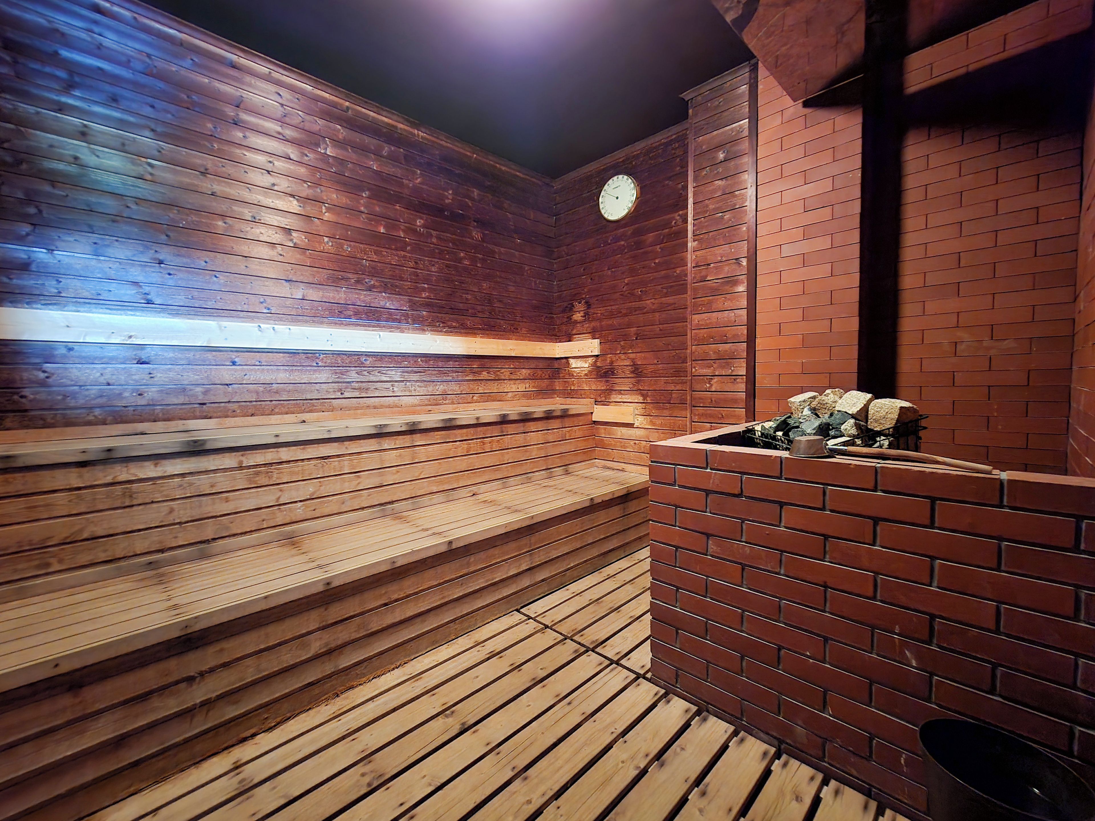 Una sauna con panche in legno e un muro in mattoni, un orologio e un braciere.