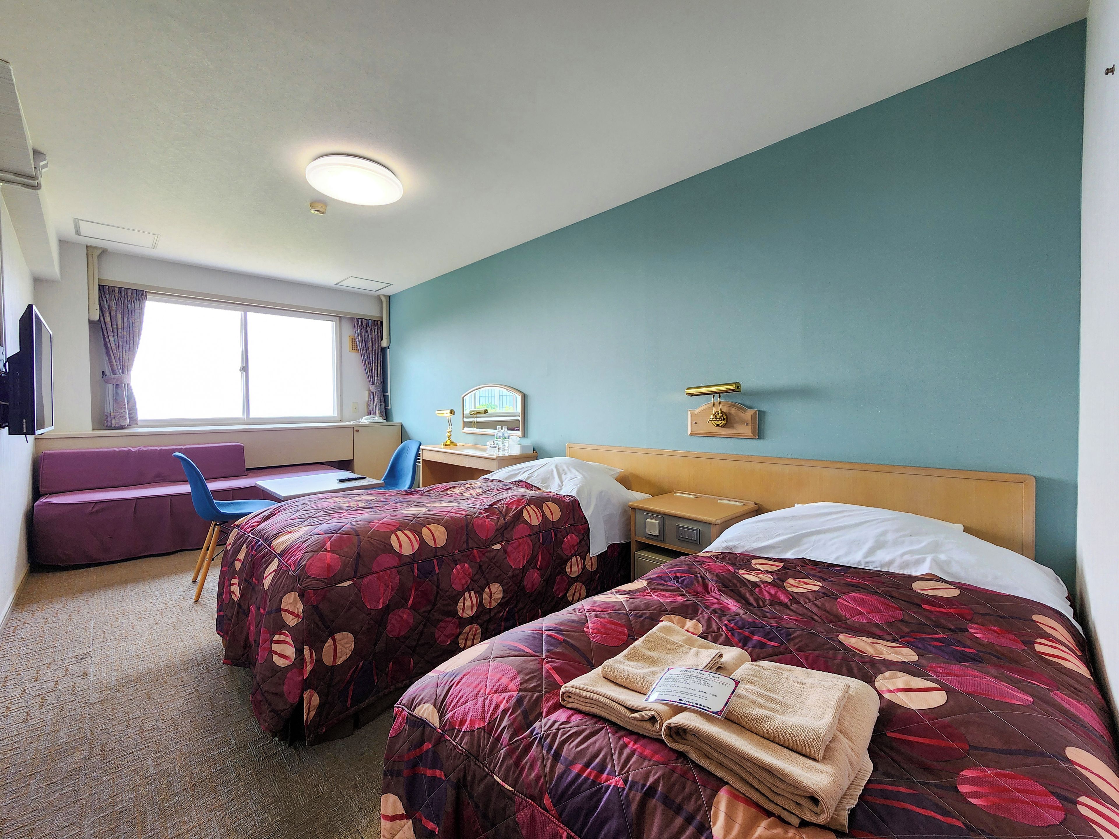 A hotel room with two beds, a desk, a chair, and a window with curtains.