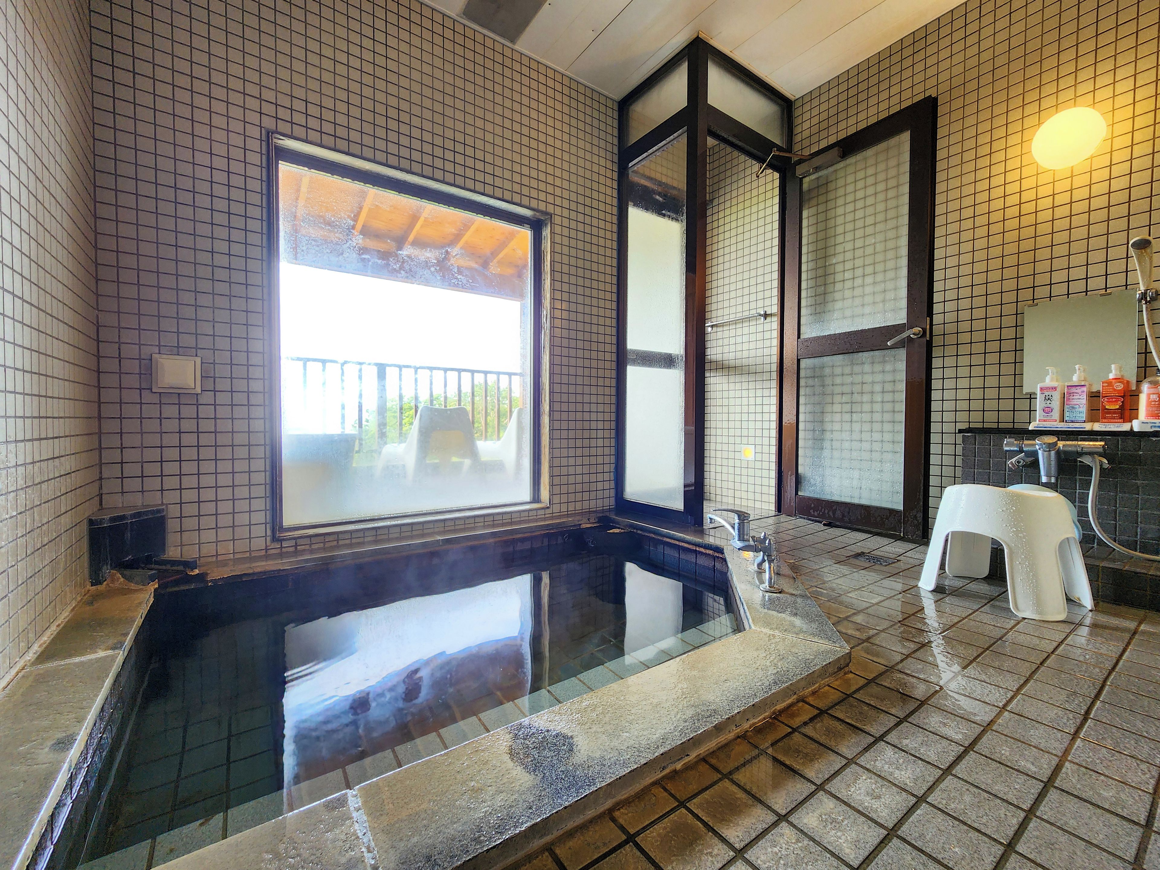 A bathroom with a glass-enclosed hot tub, a window with a view, and a tiled floor.