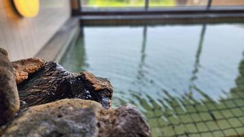 A stone wall with a water feature, a window with a view of greenery, and a tiled floor.
