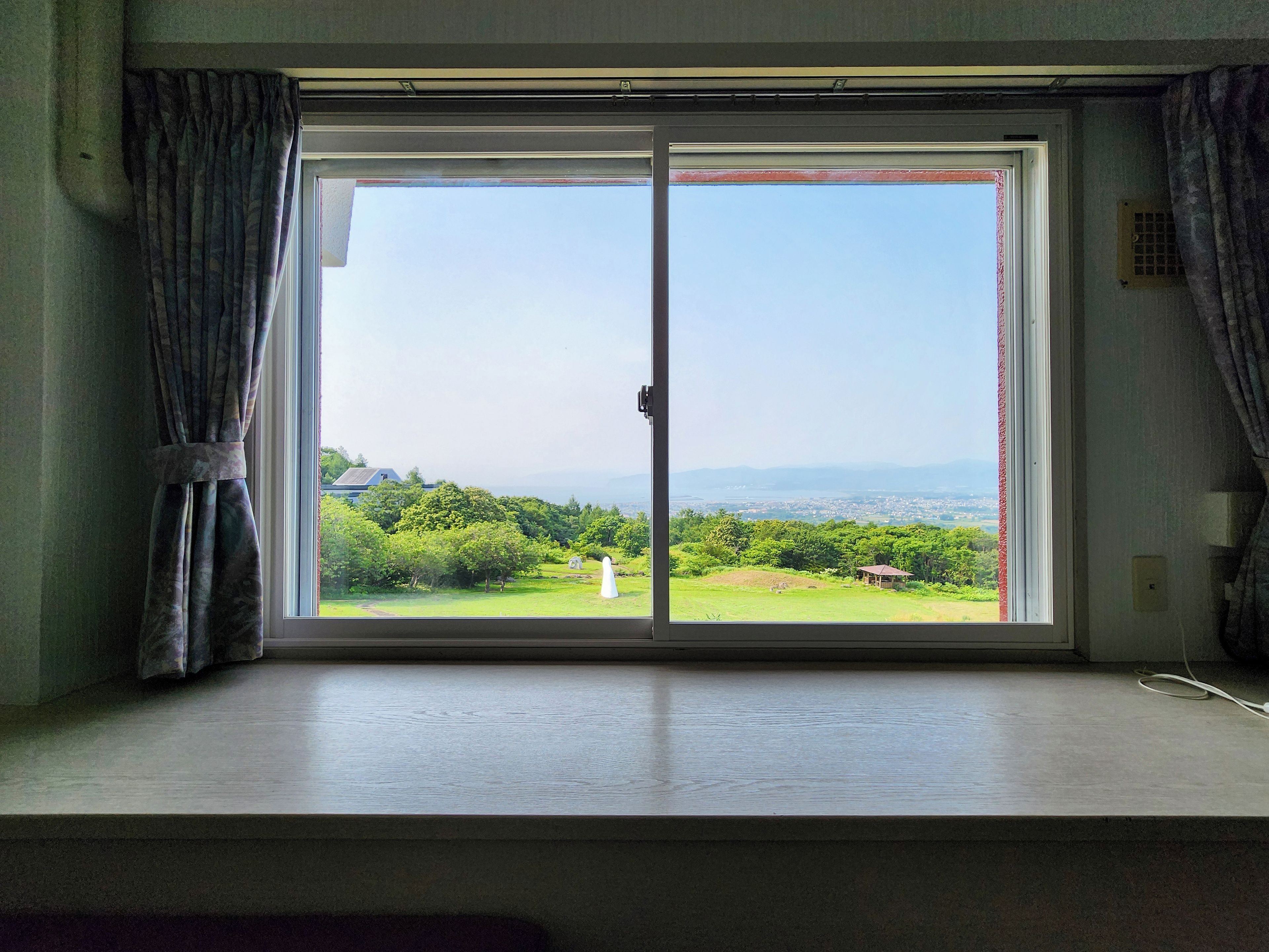 A room with a large sliding glass door leading to a view of a green landscape and distant mountains.