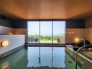 A swimming pool with a view of greenery and buildings, tiled walls, and a wooden ceiling. - Iwanai Kogen Hotel (Iwanai)
