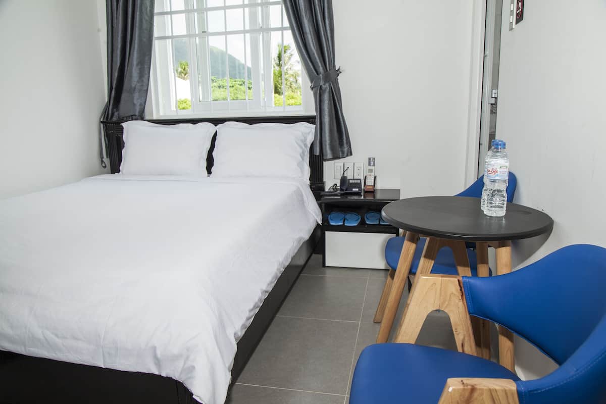 A hotel room with a bed, a small table with a chair, a water bottle, and a telephone.