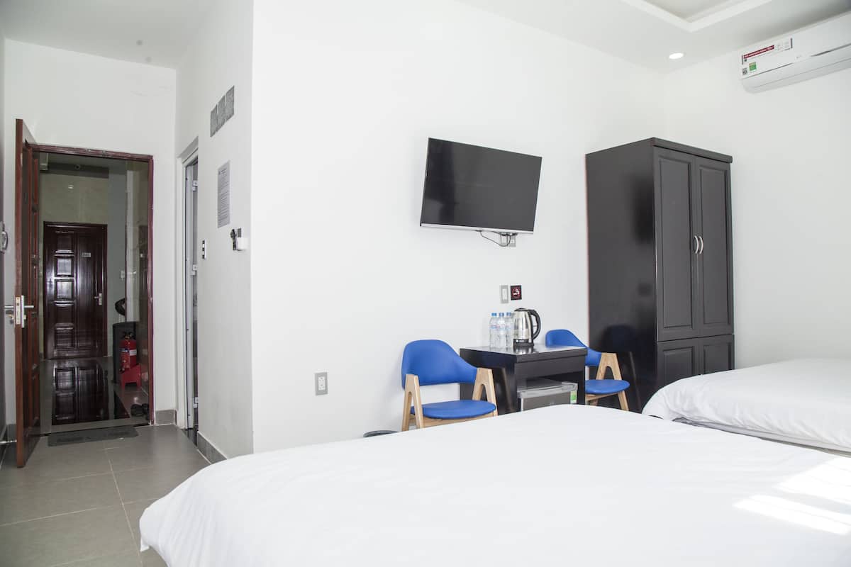 A hotel room with two beds, a TV mounted on the wall, a desk with chairs, and a wardrobe.