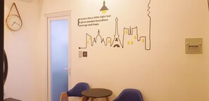 A room with a wall clock, a door, two blue chairs, a small table, and a wall decal with a cityscape and inspirational text. - Thao Lien Hotel (Ho Chi Minh City)