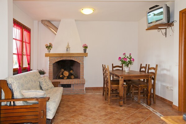 Una sala de estar con chimenea, un sofá, una mesa de comedor con sillas y una televisión montada en la pared.