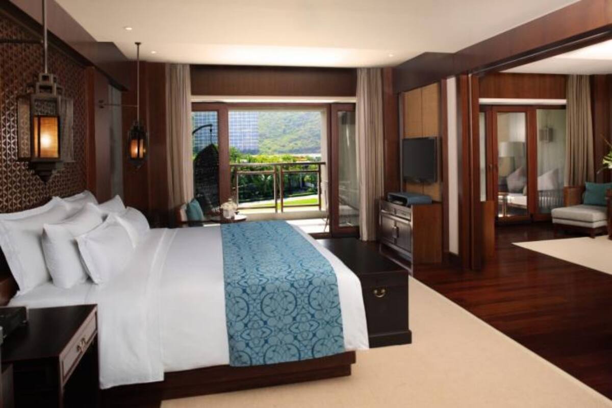 A spacious bedroom with a large bed, a desk, and a view of a lush garden through a sliding door.