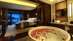 Ein Hotelzimmer mit einer großen Badewanne voller Rosenblätter, einem Bett, einem Badezimmer mit Spiegel und Blick auf die Berge.