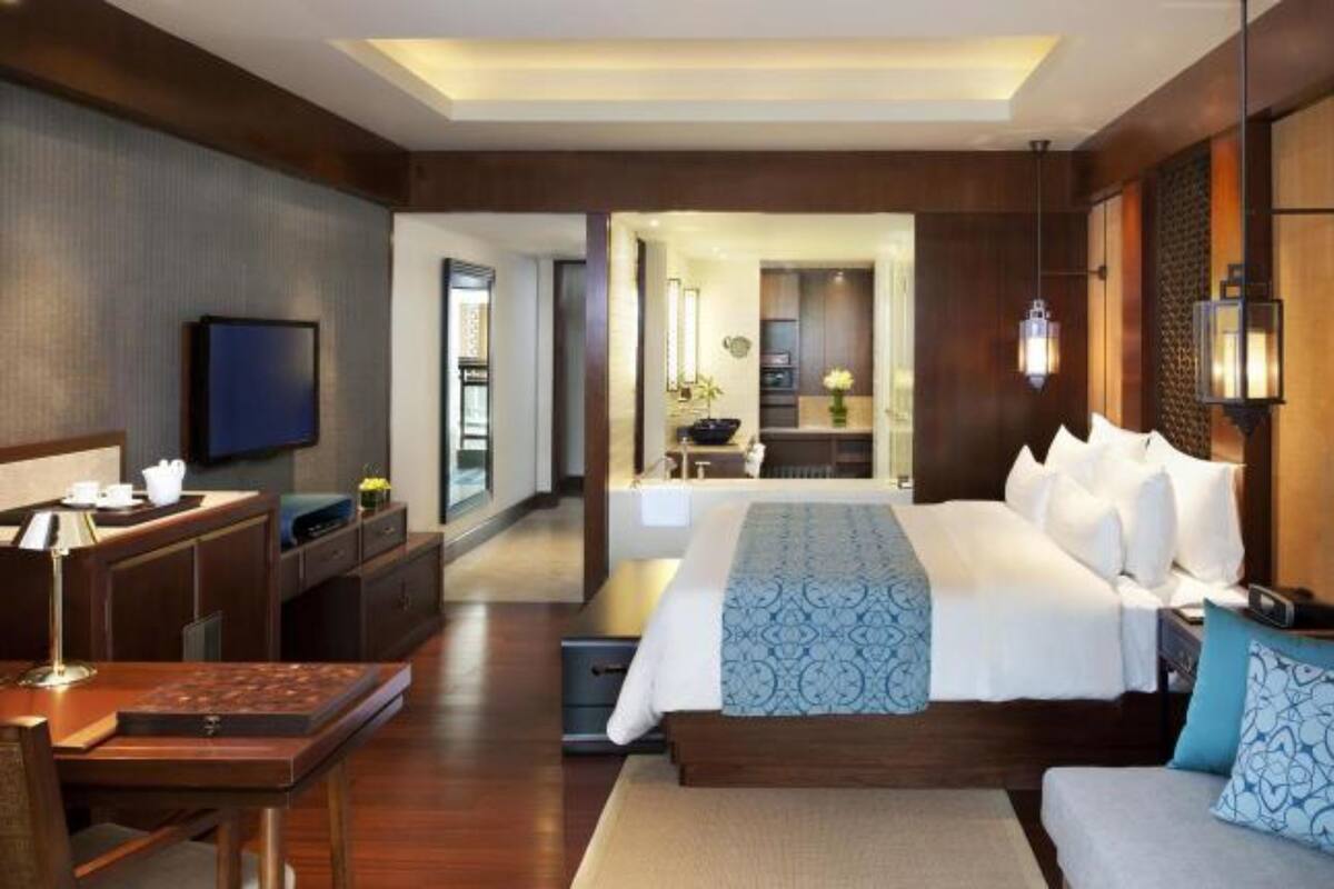 A hotel room with a large bed, a desk with a chair, a television, and a sofa.