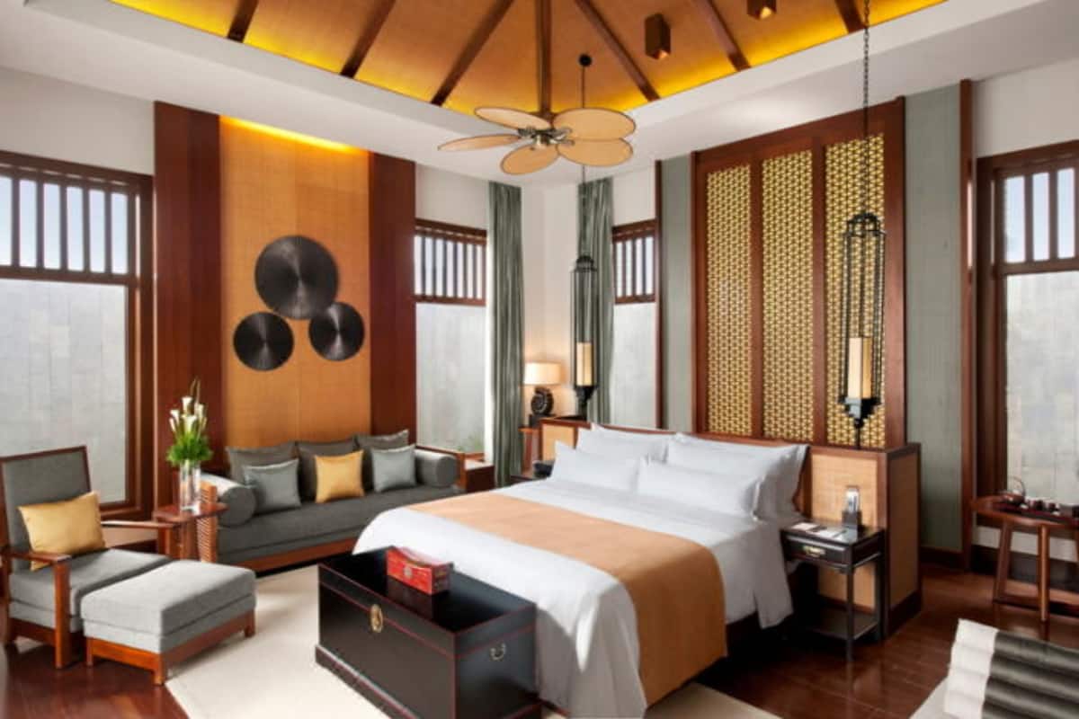 A modern hotel room with a large bed, a sofa, a desk, and a ceiling fan.