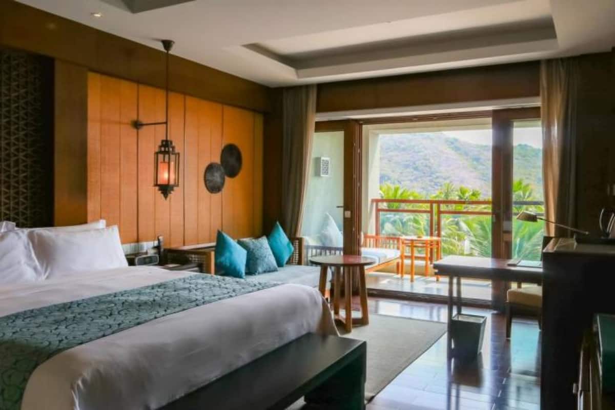 A hotel room with a large bed, a desk, and a balcony with a view of the mountains.