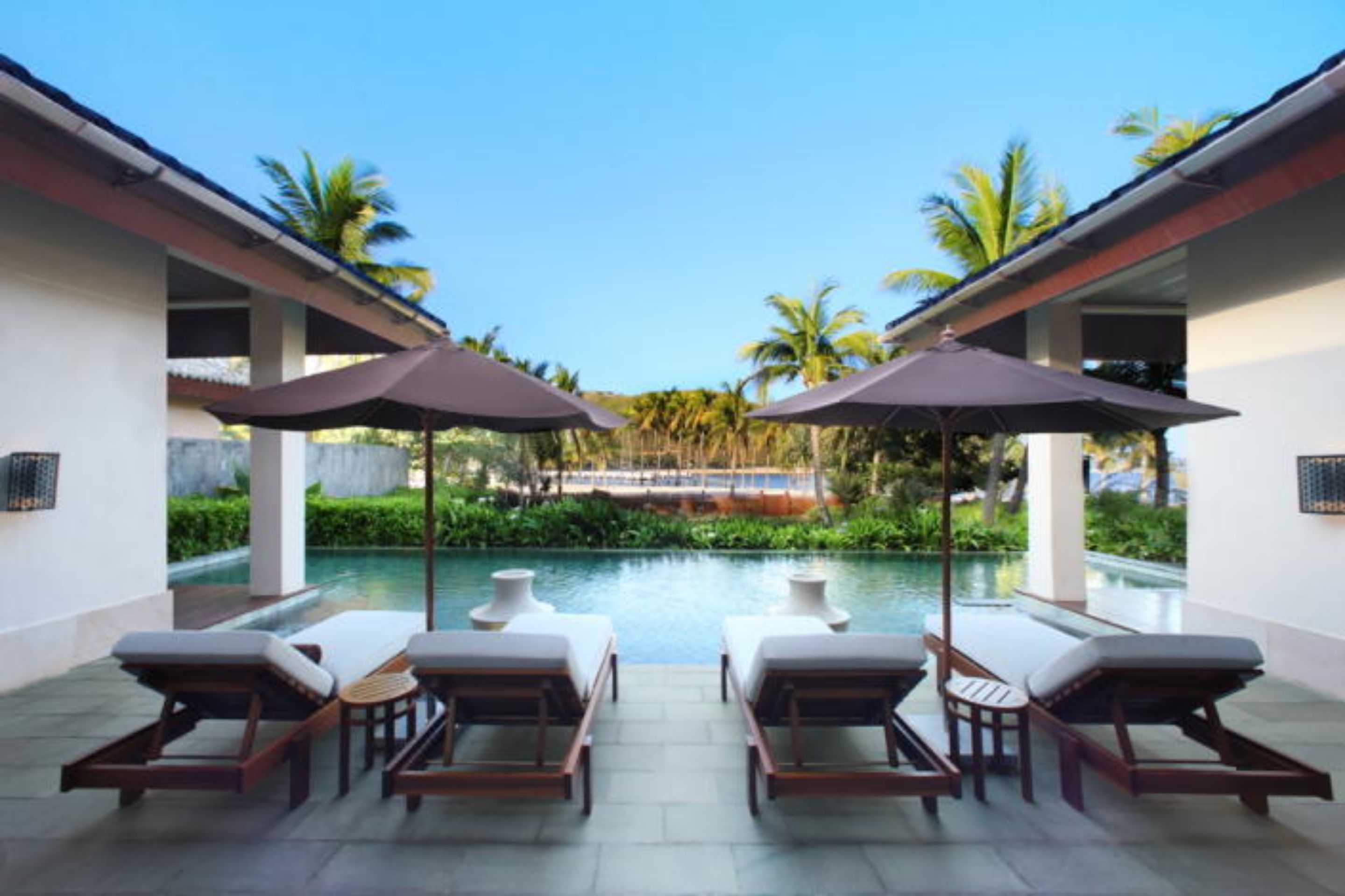 A poolside area with lounge chairs and umbrellas, a clear view of the pool, and a tropical garden backdrop.