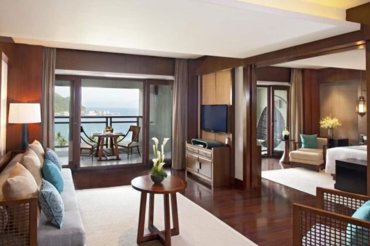 A spacious hotel room with a balcony, a dining area, and a TV.