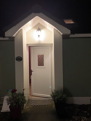 A house with a white door, a small porch, and a light fixture above the door. - Peaceful cottage with sea & mountain views - pet-friendly (Ballycastle)