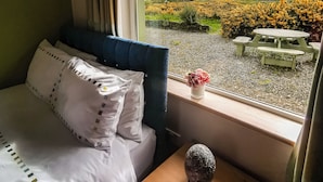 A bedroom with a bed, a wooden nightstand, a window with a view of a field and hills.