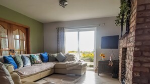 A living room with a beige sectional sofa, a patterned rug, a brick fireplace, and a view through a glass door.